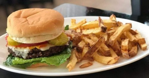 A juicy hamburger with lettuce, tomato, pickles, and fries on a white plate.