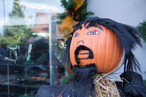 A scarecrow with a pumpkin head, painted facial features, and a straw body, decorated for a festive display.