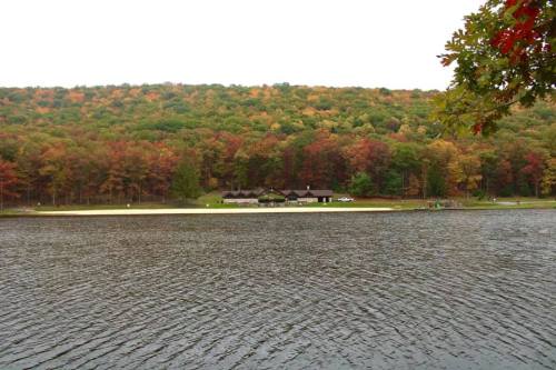 A serene lake scene with a forested hillside displaying autumn colors and a small building along the shore.