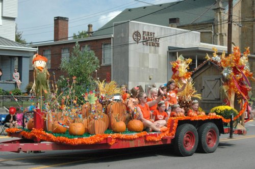 A colorful parade float decorated with pumpkins, flowers, and autumn themes, featuring children in festive attire.
