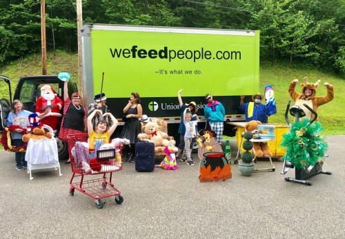 A group of people in costumes and props poses in front of a green truck, surrounded by toys and decorations.