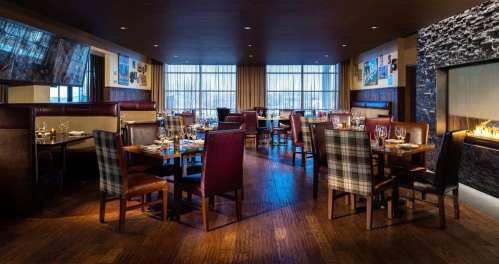 Cozy restaurant interior with wooden floors, elegant seating, and a fireplace, featuring tables set for dining.