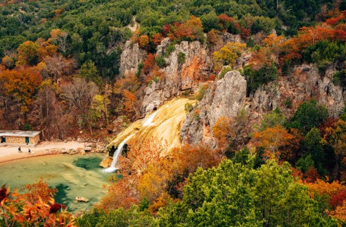A scenic view of a waterfall cascading into a turquoise pool, surrounded by vibrant autumn foliage and rocky cliffs.
