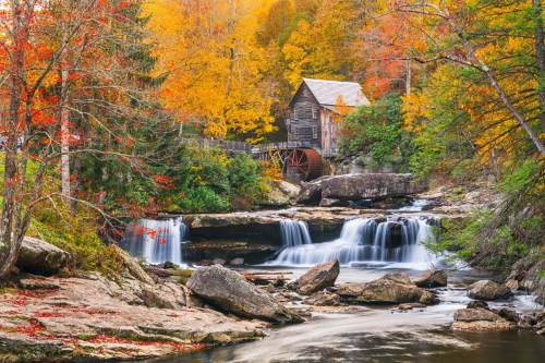 A scenic view of a historic watermill surrounded by vibrant autumn foliage and flowing waterfalls.