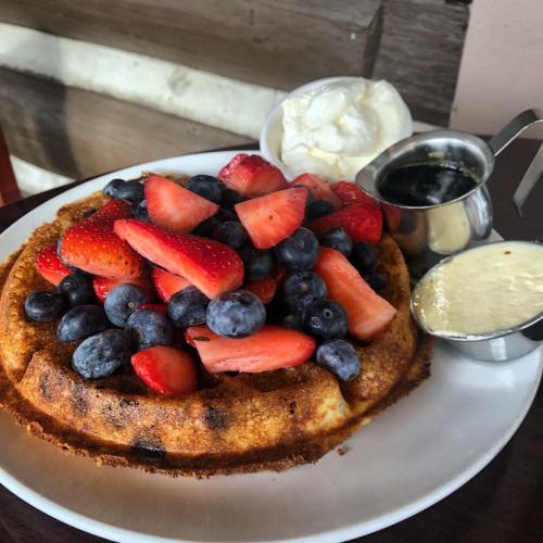 A golden waffle topped with fresh strawberries and blueberries, served with whipped cream and syrup on the side.