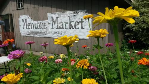 Colorful flowers in the foreground with a rustic sign reading "Mentone Market" in the background.