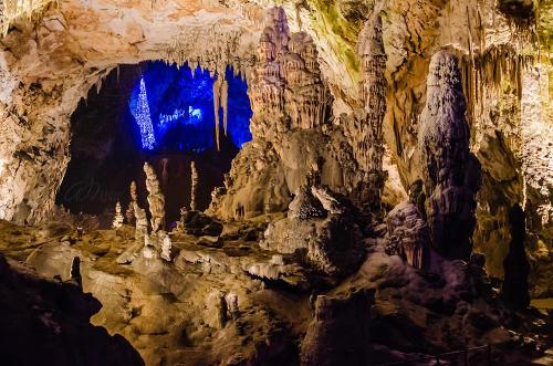 A stunning cave interior with stalactites and stalagmites, illuminated by blue and warm lights.