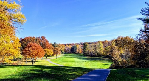 A scenic view of a golf course surrounded by vibrant autumn trees under a clear blue sky.