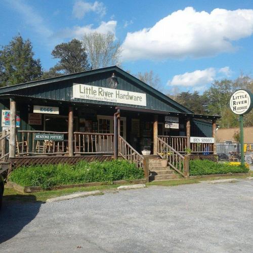 A rustic hardware store with a wooden porch, surrounded by trees and a blue sky, featuring a sign that reads "Little River Hardware."