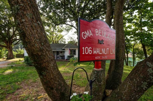 A red sign reading "GMA BEULAH'S 106 WALNUT LN est. 2020" stands near a house surrounded by trees.