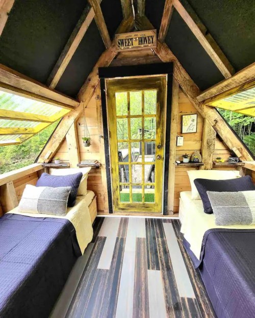 Cozy cabin interior with two beds, wooden accents, and a bright yellow door leading to a scenic view.
