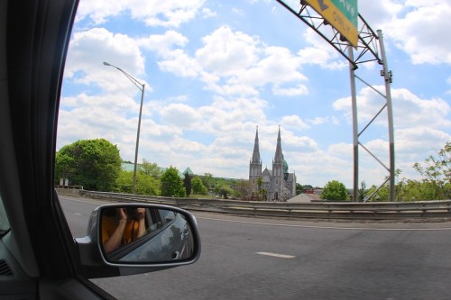 View from a car window showing a church with tall spires and a cloudy sky in the background.