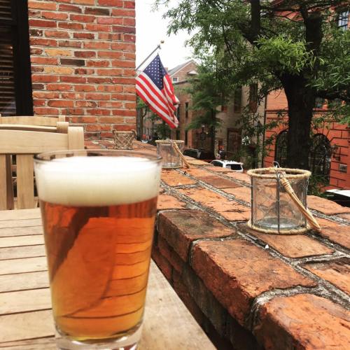 A glass of beer sits on a brick ledge, with an American flag and a street view in the background.