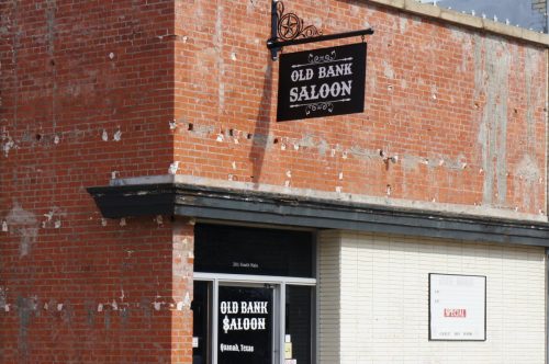 Exterior of the Old Bank Saloon, featuring a brick facade and a sign, located in a small Texas town.