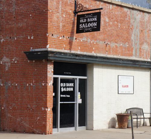 Exterior of the Old Bank Saloon, featuring a brick facade and a sign, located in a small Texas town.