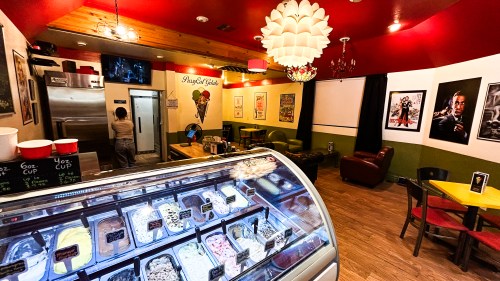 A cozy ice cream shop with colorful decor, featuring a display of ice cream flavors and a customer in the background.