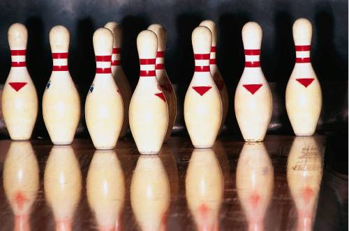 A set of bowling pins arranged in a triangle formation, reflecting on a polished wooden surface.