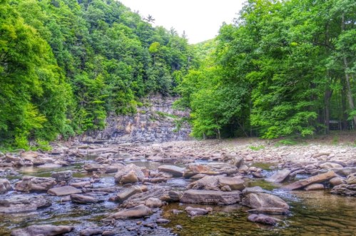 A serene river flows through a rocky landscape, surrounded by lush green trees and steep cliffs.