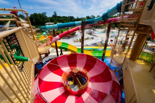 A colorful water park featuring slides, a spiral slide, and a splash area under a bright blue sky.