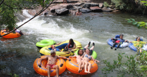 A group of people relax on colorful inner tubes in a river, surrounded by rocks and greenery.