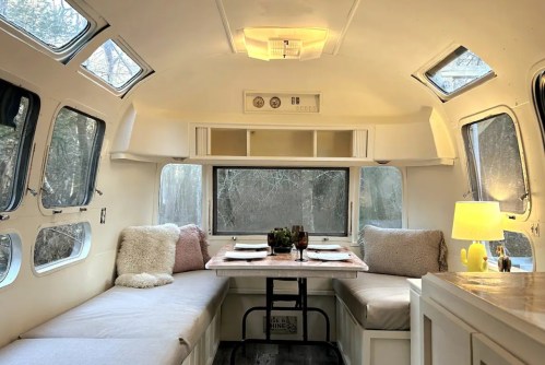 Cozy interior of a vintage Airstream with a dining area, soft cushions, and large windows letting in natural light.