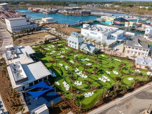 Aerial view of a mini-golf course with green turf and white sand traps, surrounded by buildings and a marina.