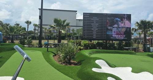 A mini-golf course with a scoreboard and palm trees in the background on a sunny day.