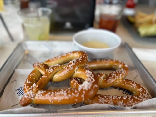 A close-up of soft pretzels sprinkled with salt, served on a tray with a small bowl of dipping sauce.