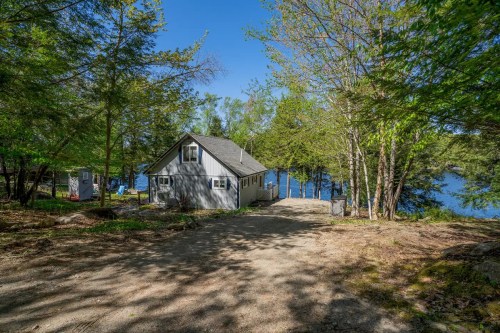 A cozy house surrounded by trees near a serene lake on a sunny day.