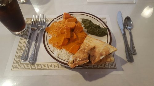 A plate of rice topped with orange curry, sweet potatoes, a green sauce, and pieces of flatbread, with utensils and a drink.