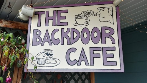 Sign for "The Backdoor Cafe" featuring illustrations of coffee, pastries, and a steaming cup.
