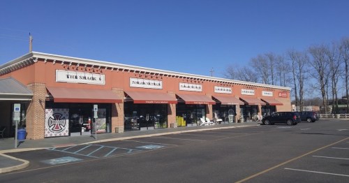 A row of storefronts with awnings, featuring "The Shack" and other businesses, under a clear blue sky.