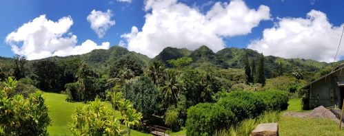 Lush green mountains under a bright blue sky with fluffy clouds, surrounded by tropical vegetation.