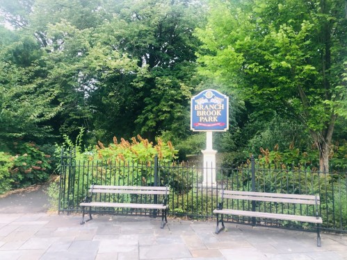 Sign for Branch Brook Park surrounded by lush greenery and two empty benches in a peaceful setting.