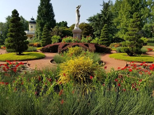 A beautifully landscaped garden featuring colorful flowers, lush greenery, and a central statue surrounded by vibrant plants.