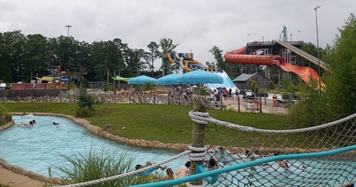 A water park scene featuring slides, a lazy river, and visitors enjoying the attractions on a cloudy day.