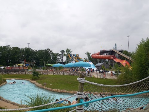 A water park scene featuring slides, a lazy river, and visitors enjoying the attractions under a cloudy sky.