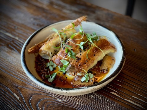 A plate of crispy fried dumplings garnished with microgreens, served with a drizzle of sauce on a wooden table.