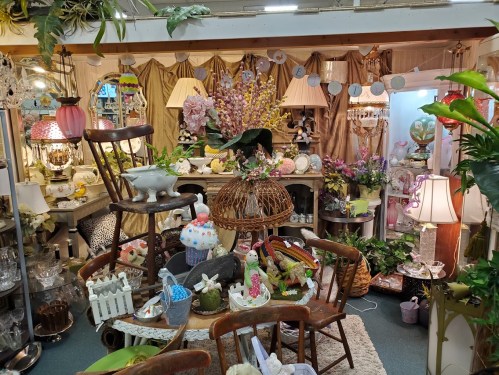 A cozy vintage shop display filled with decorative items, lamps, plants, and colorful Easter decorations.