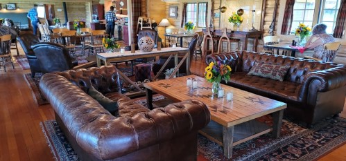 Cozy interior of a rustic lodge with leather sofas, wooden tables, and sunflowers, creating a warm, inviting atmosphere.