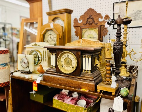A collection of vintage clocks and decorative items displayed on a wooden shelf in an antique shop.
