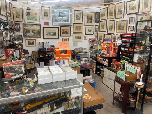 A cluttered antique shop filled with framed artwork, collectibles, and various vintage items on display.