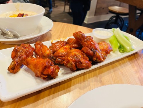 A platter of crispy chicken wings with a side of celery and dipping sauce on a wooden table.
