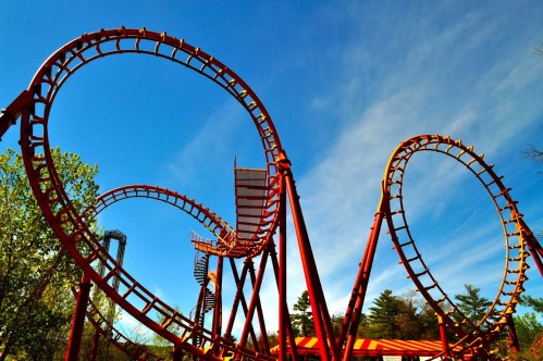 A vibrant roller coaster with loops against a clear blue sky, surrounded by trees.