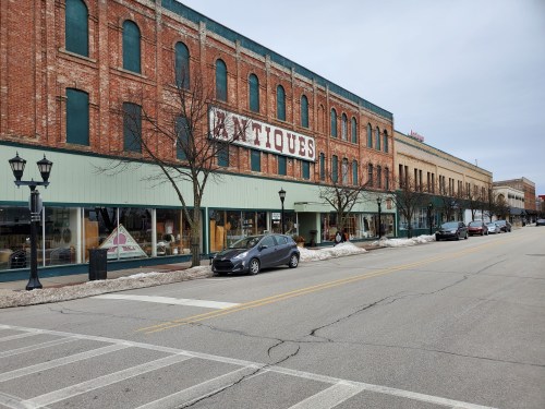 A street view of a brick building with an "Antiques" sign, featuring parked cars and bare trees in winter.