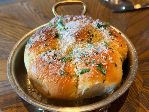 A golden, cheesy bread roll topped with herbs and grated cheese, served in a small metal dish.