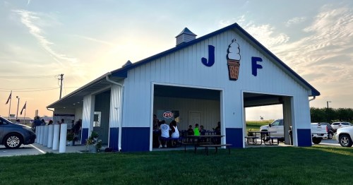 A blue and white ice cream shop with outdoor seating, people enjoying treats, and a sunset in the background.