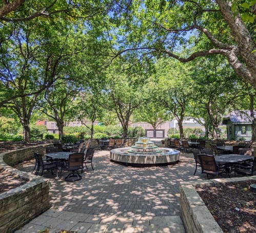 A serene outdoor space with a circular stone fountain surrounded by trees and seating areas.