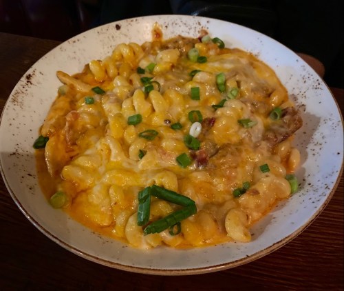A creamy pasta dish topped with melted cheese and green onions, served in a white bowl.