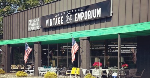 Exterior of Newburgh Vintage Emporium with American flags, colorful outdoor furniture, and a sign displaying the store name.